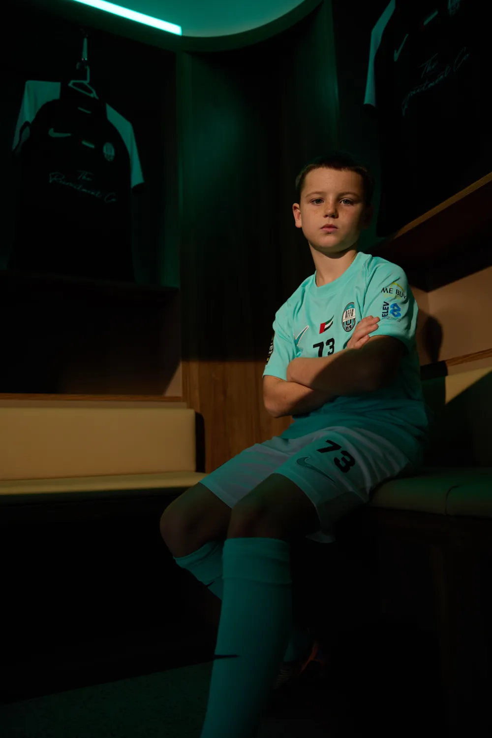Arabian Falcons Academy player in official club kit, seated in the dressing room