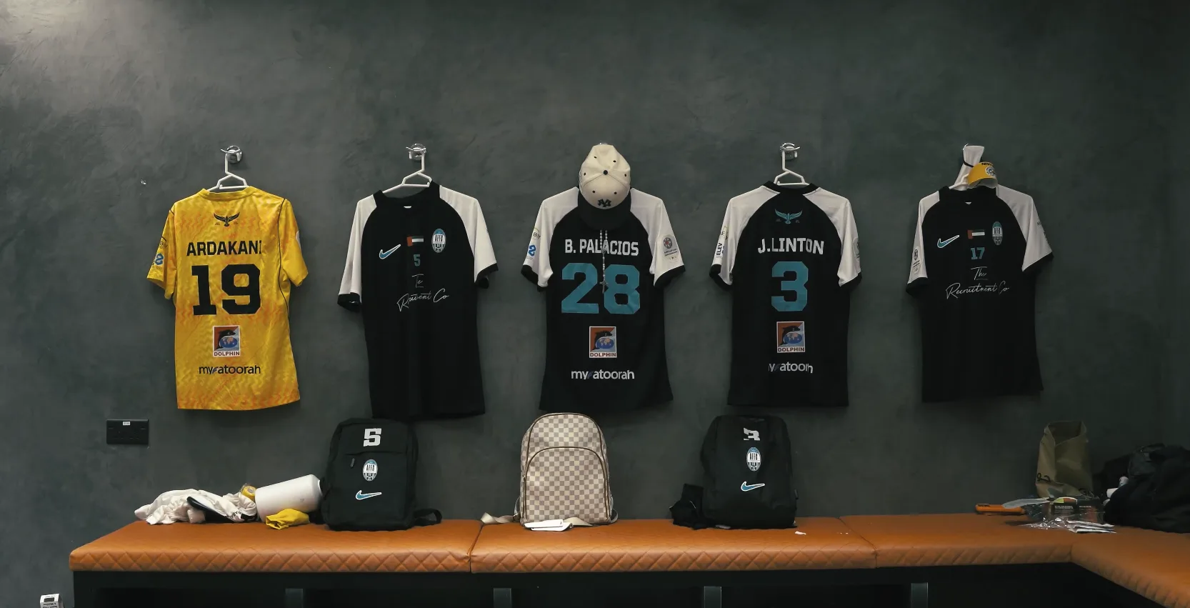 Official Arabian Falcons FC match shirts with partner branding hanging in the club dressing room